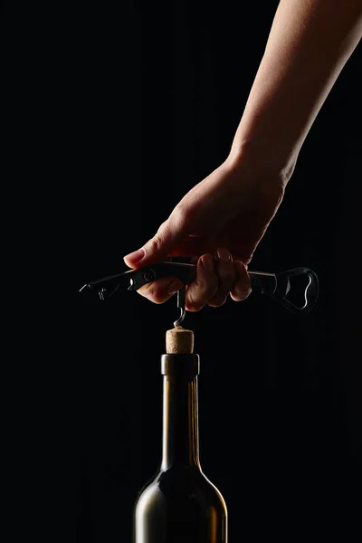 Cropped view of woman opening wine bottle with corkscrew isolated on black — Stock Photo