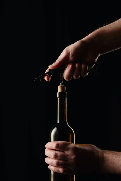 Vista parcial del hombre abriendo botella de vino con sacacorchos aislados en negro - foto de stock