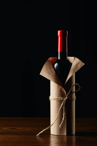 Wine bottle in paper wrapper on wooden surface isolated on black — Stock Photo