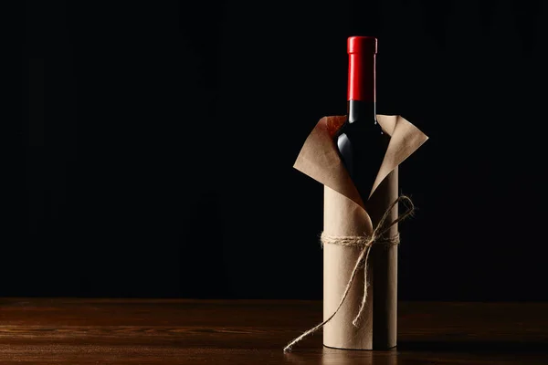 Bottiglia di vino in involucro di carta su superficie di legno isolata su nero — Foto stock