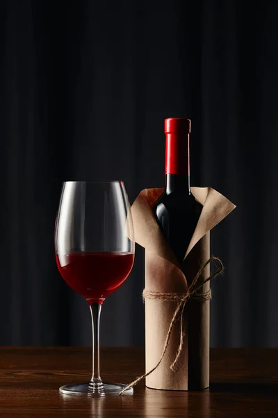 Copo de vinho e garrafa em papel de embrulho na superfície de madeira — Fotografia de Stock