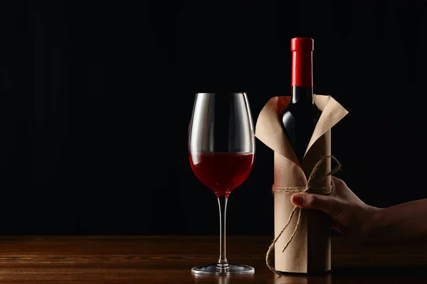 Partial view of woman holding wine bottle in paper wrapper — Stock Photo