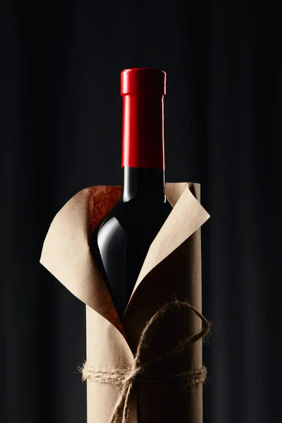 Botella de vino de vidrio en papel envoltorio en la oscuridad - foto de stock