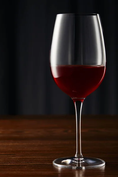 Bicchiere di vino con vino rosso su superficie di legno al buio — Foto stock