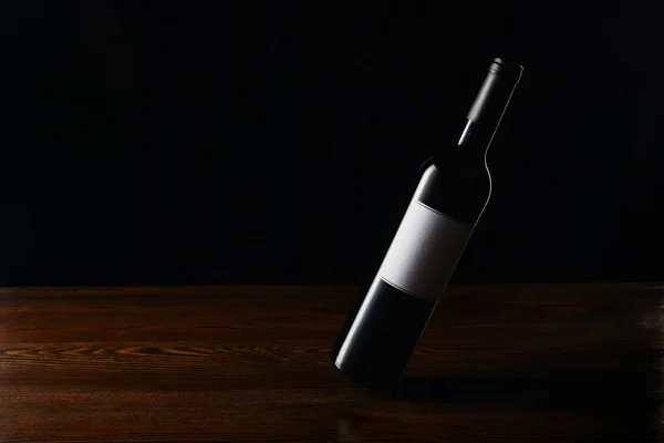 Wine bottle with blank label on wooden surface isolated on black — Stock Photo