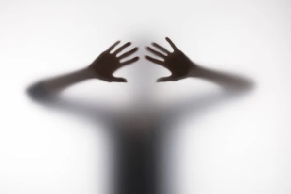 Blurry silhouette of person touching glass with hands — Stock Photo