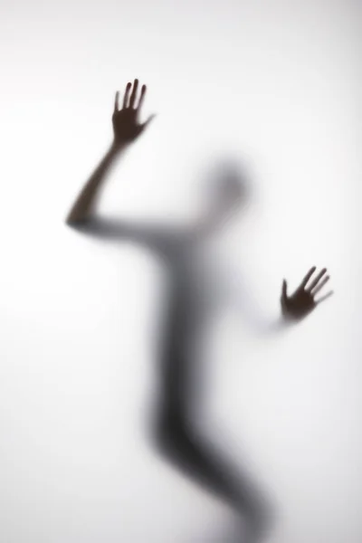 Blurry silhouette of person touching glass with hands — Stock Photo