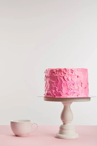 Rosa leckere gebackene Geburtstagstorte auf Kuchenständer in der Nähe Tasse isoliert auf grau — Stockfoto