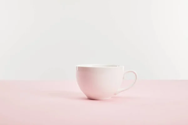 Біла чашка з напоєм на рожевій поверхні ізольована на сірому — стокове фото