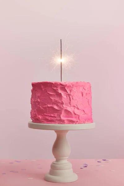 Delicious pink birthday cake with sparkler on cake stand isolated on pink — Stock Photo