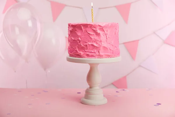 Sabroso pastel de cumpleaños rosa con vela ardiente en pie de la torta cerca de globos de aire y decoración — Stock Photo