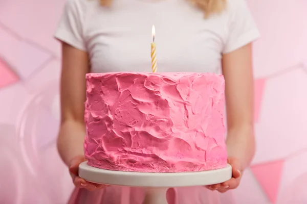 Close up de mulher segurando bolo stand com doce bolo de aniversário rosa e vela ardente — Fotografia de Stock