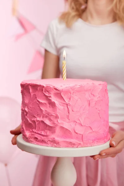 Foco seletivo da mulher segurando carrinho de bolo com bolo de aniversário rosa saboroso e vela acesa — Fotografia de Stock