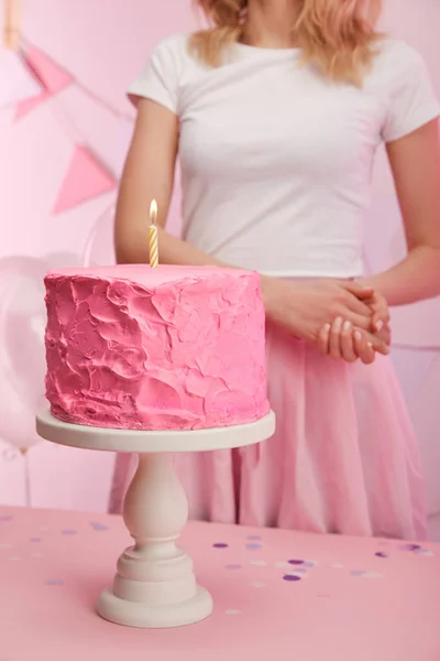 Cropped view of woman standing near baked tasty birthday cake with burning candle on cake stand — Stock Photo