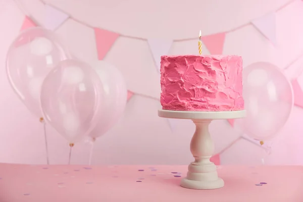 Gâteau d'anniversaire sucré et savoureux avec bougie allumée sur le stand de gâteau près de ballons à air et décoration — Photo de stock