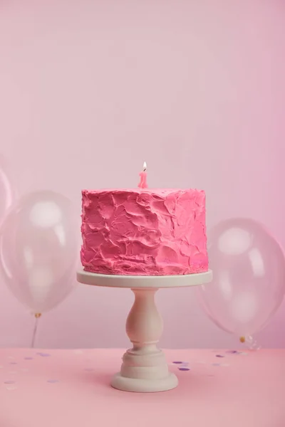 Queimando vela número um no bolo de aniversário rosa e saboroso no suporte de bolo perto de balões de ar no rosa — Fotografia de Stock