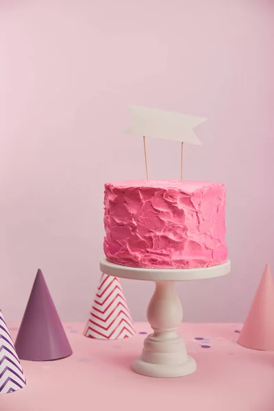 Pastel de cumpleaños sabroso y dulce con tarjeta en blanco cerca de gorras de fiesta en rosa - foto de stock