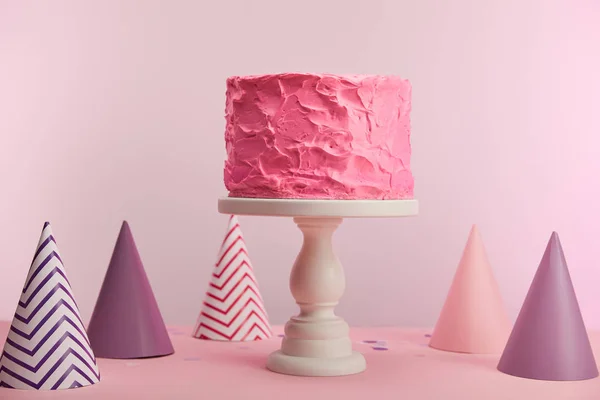 Tasty and sweet birthday cake near party caps on pink — Stock Photo