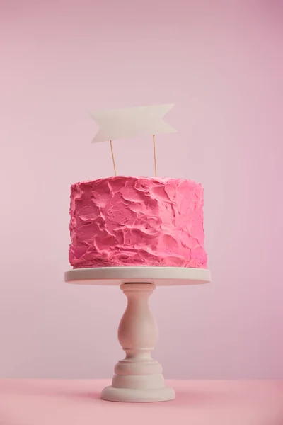 Gâteau d'anniversaire savoureux et sucré avec carte blanche sur support de gâteau sur rose — Photo de stock