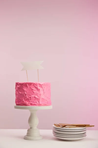 Pastel de cumpleaños sabroso y dulce con tarjeta en blanco en pie de la torta cerca de platillos blancos y tenedores de oro en rosa — Stock Photo