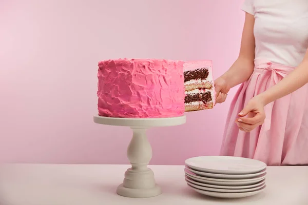 Vue recadrée de la femme prenant morceau de gâteau d'anniversaire doux près de soucoupes blanches sur rose — Photo de stock