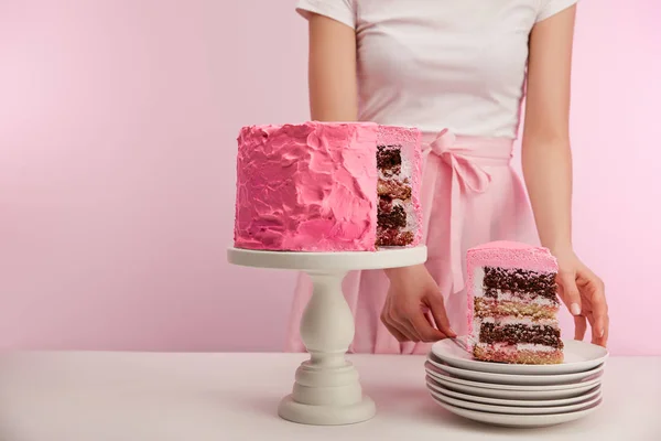 Cropped view of woman standing near piece of sweet pink birthday cake in white saucer on pink — Stock Photo