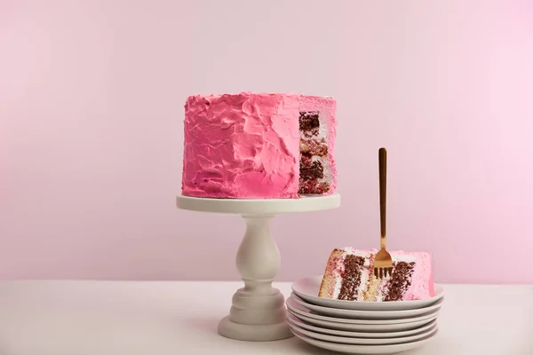 Piece of sweet pink birthday cake with golden fork in white saucer on pink — Stock Photo