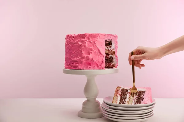 Vista cortada de mulher segurando garfo dourado em pedaço de bolo de aniversário doce em disco branco em rosa — Fotografia de Stock