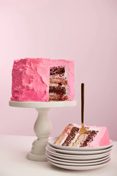 Piece of sweet birthday cake with golden fork in white saucer on pink — Stock Photo
