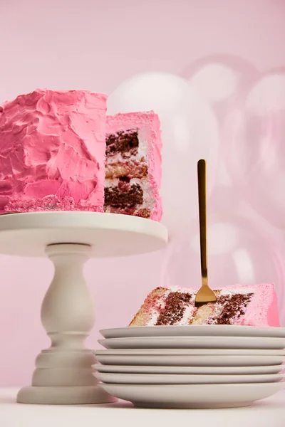 Вид знизу шматка смачного торта на день народження з золотою вилкою в білій тарілці біля повітряних кульок на рожевому — стокове фото