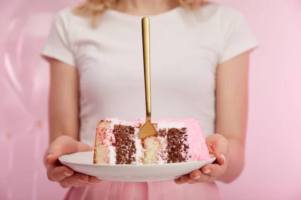 Foco selectivo de plato con trozo de sabroso pastel de cumpleaños y tenedor de oro en manos de la mujer - foto de stock