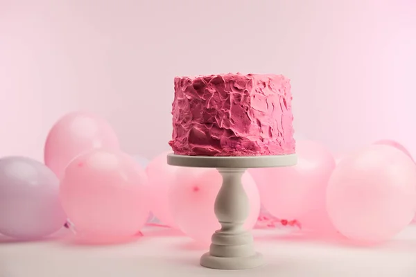 Selective focus of tasty pink birthday cake on cake stand near air balloons on pink — Stock Photo