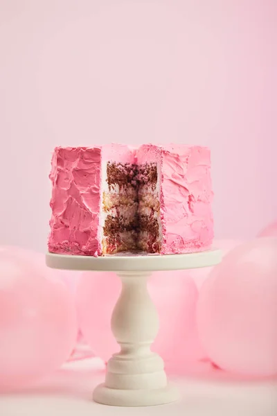 Selective focus of tasty cut birthday cake on cake stand near air balloons on pink — Stock Photo