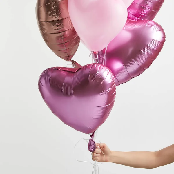 Vista parcial de la niña sosteniendo globos de aire rosa en forma de corazón aislados en blanco - foto de stock
