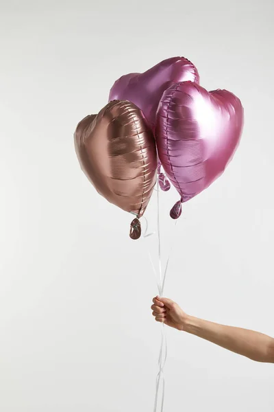 Vista parcial de la niña sosteniendo globos de aire rosa en forma de corazón aislados en blanco con espacio de copia - foto de stock