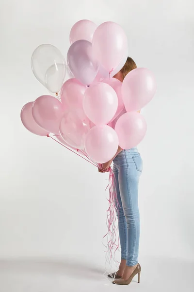 Девушка на высоких каблуках и джинсовой покрывающей лицо розовыми воздушными шарами на белом — стоковое фото