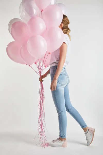 Fille en vêtements décontractés couvrant le visage avec des ballons d'air rose festive sur blanc — Photo de stock