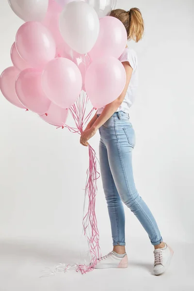 Дівчина в повсякденному одязі, що покриває обличчя рожевими повітряними кульками на білому — стокове фото