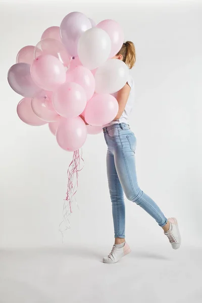 Ragazza in abiti casual che copre il viso con palloncini rosa su bianco — Foto stock