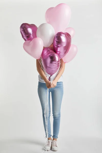 Girl in denim covering face with heart-shaped pink air balloons on white — Stock Photo