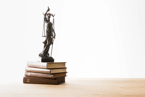 Bronze figurine with scales of justice on brown books on wooden table isolated on white — Stock Photo