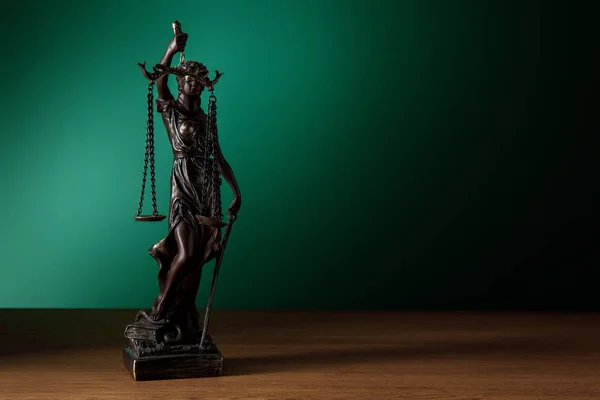 Statuette en bronze avec des écailles de justice sur une surface en bois sur fond vert foncé — Photo de stock