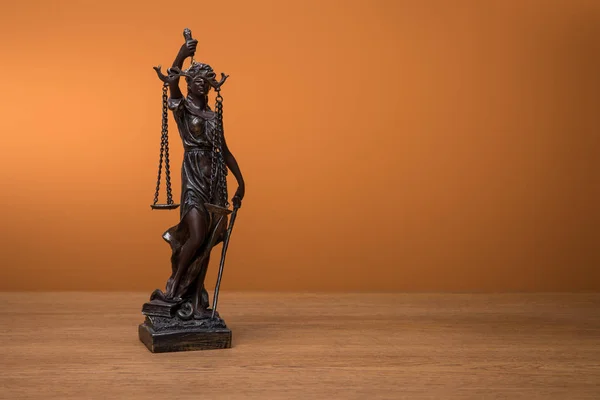 Bronze statuette with scales of justice on wooden table on orange background — Stock Photo