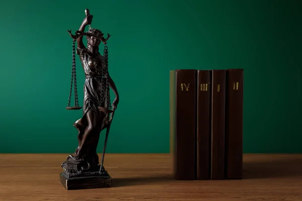 Statuette en bronze avec des échelles de justice et des volumes de livres bruns sur table en bois sur fond vert foncé — Photo de stock