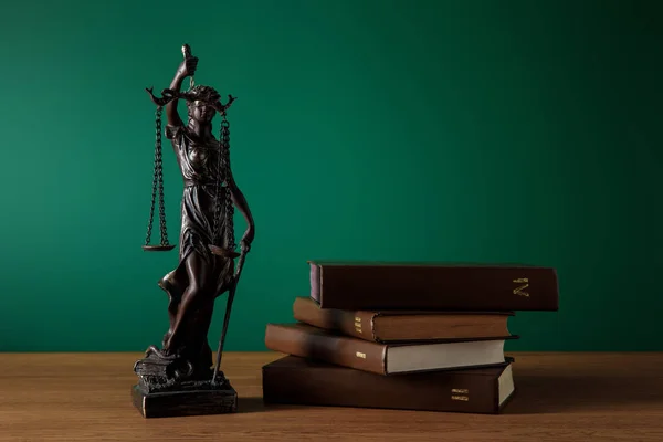Statuette en bronze avec écailles de justice et volumes de livres sur table en bois sur fond vert foncé — Photo de stock