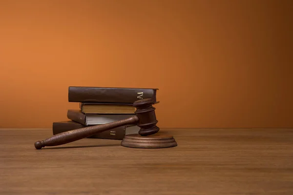 Volumes of brown books in leather covers and gavel on wooden table on dark orange background — Stock Photo