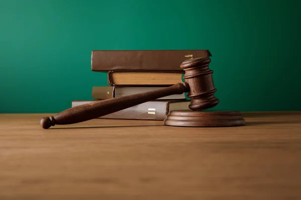 Bottom view of volumes of brown books in leather covers and gavel on wooden table on dark green background — Stock Photo