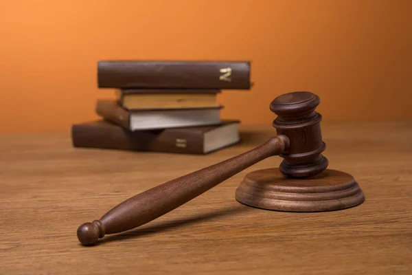 Selective focus of volumes of brown books in leather covers and wooden gavel on table on orange background — Stock Photo