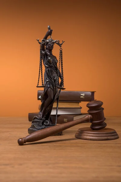 Bronze statuette with scales of justice, gavel and books on wooden table on orange background — Stock Photo