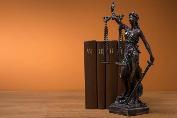 Bronzestatuette mit Maßstäben der Gerechtigkeit und Reihe brauner Bücher auf dem Tisch — Stockfoto